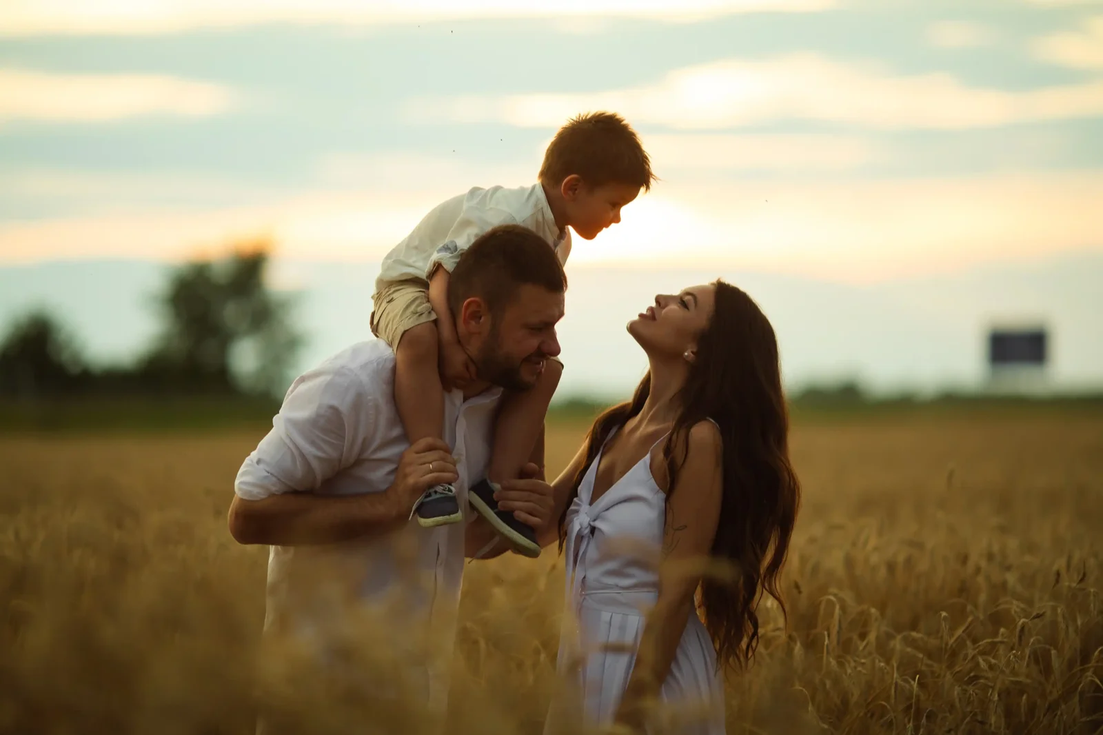 Pai com filho nos ombros e mãe sorrindo ao ar livre